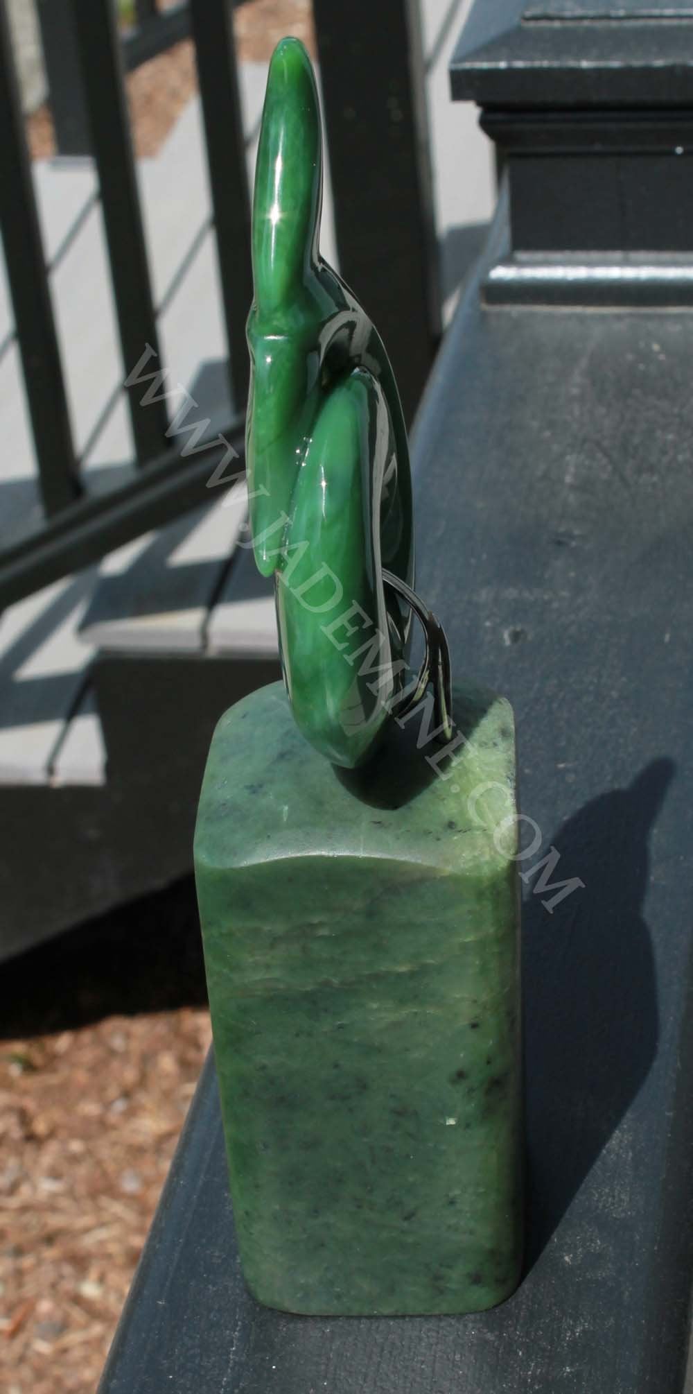 Vertical green jade whale tail sculpture viewed from the side atop a square jade base.