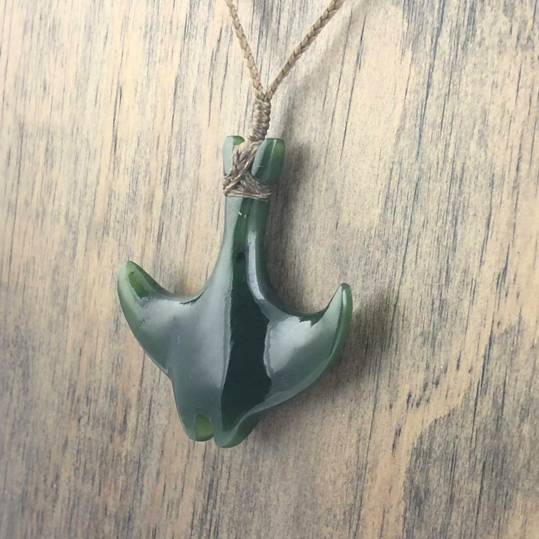 Close up of green jade manta ray pendant with wrapped cord and beads on a wood surface