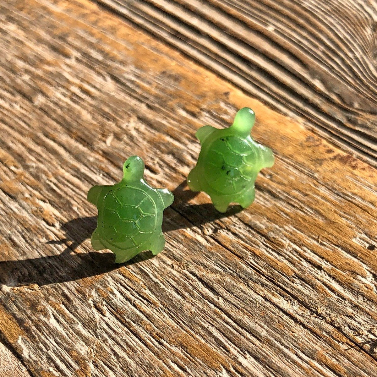 Two green turtle shaped earrings resting on a weathered wooden surface