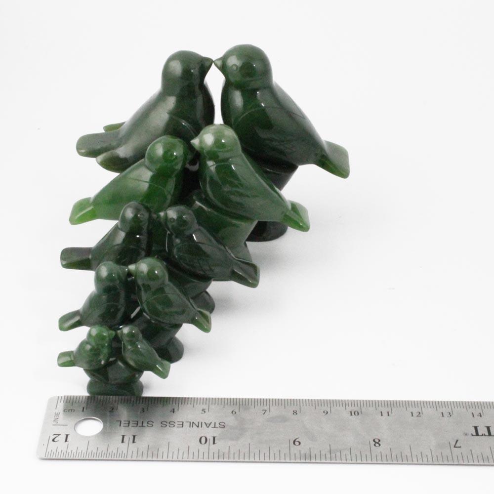Group of green jade lovebird figurines stacked along a curved stem with a ruler for scale