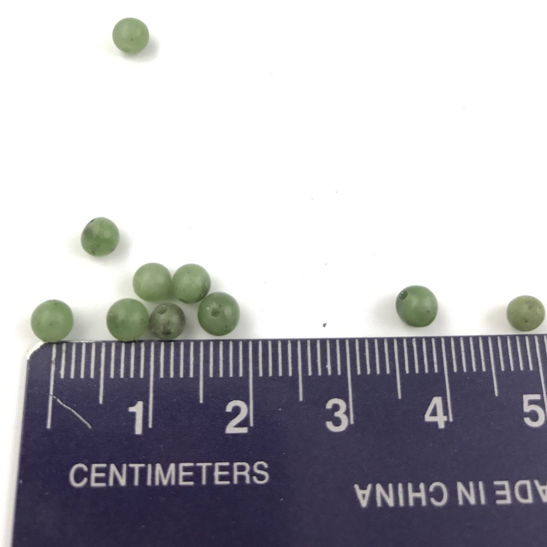 Small green jade beads 3-4 mm beside a centimeter ruler on white background