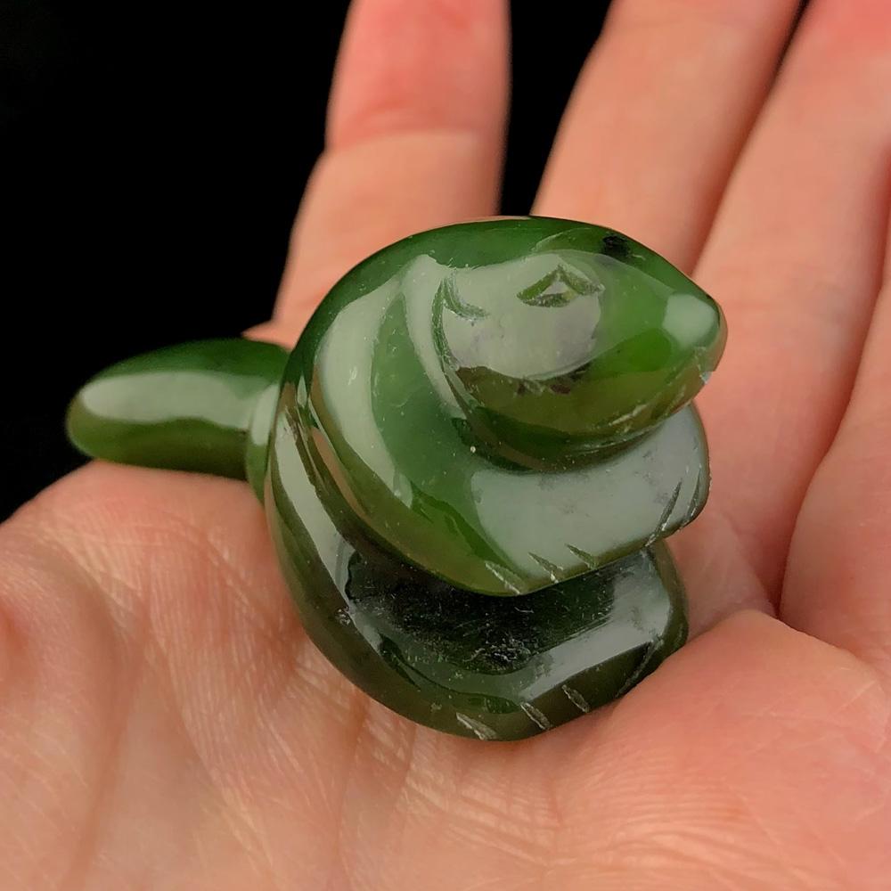 Green nephrite jade beaver carving held between fingers.