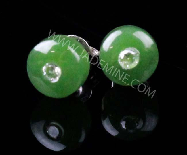 Close-up of emerald-green round stud earrings with a small central crystal on a black background