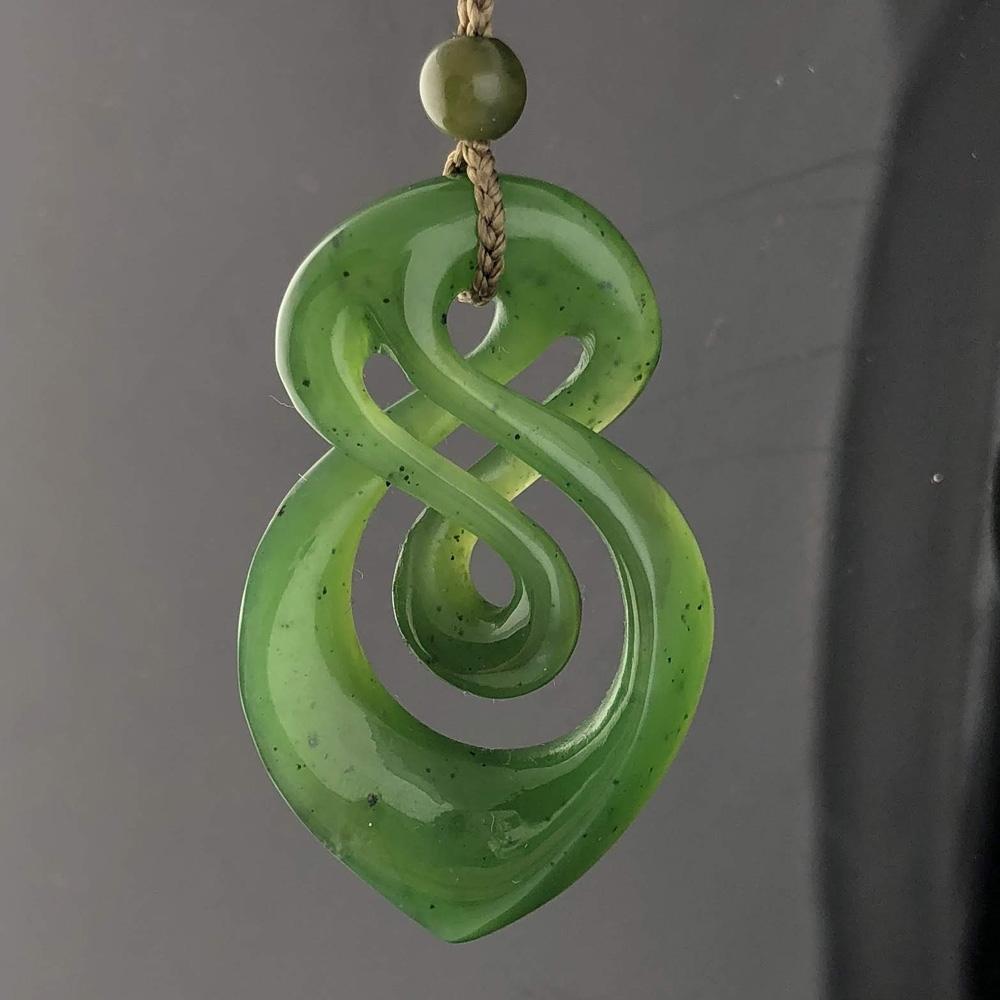 Green jade infinity twist pendant hanging from a braided cord with a small bead above.