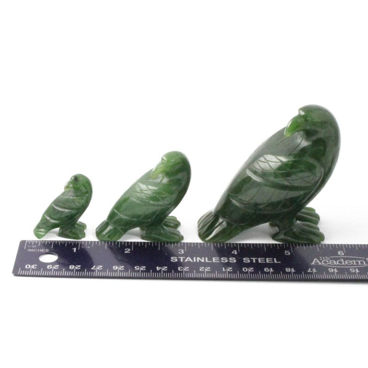 Three green jade eagle figurines in small to large sizes beside a stainless steel ruler for scale.