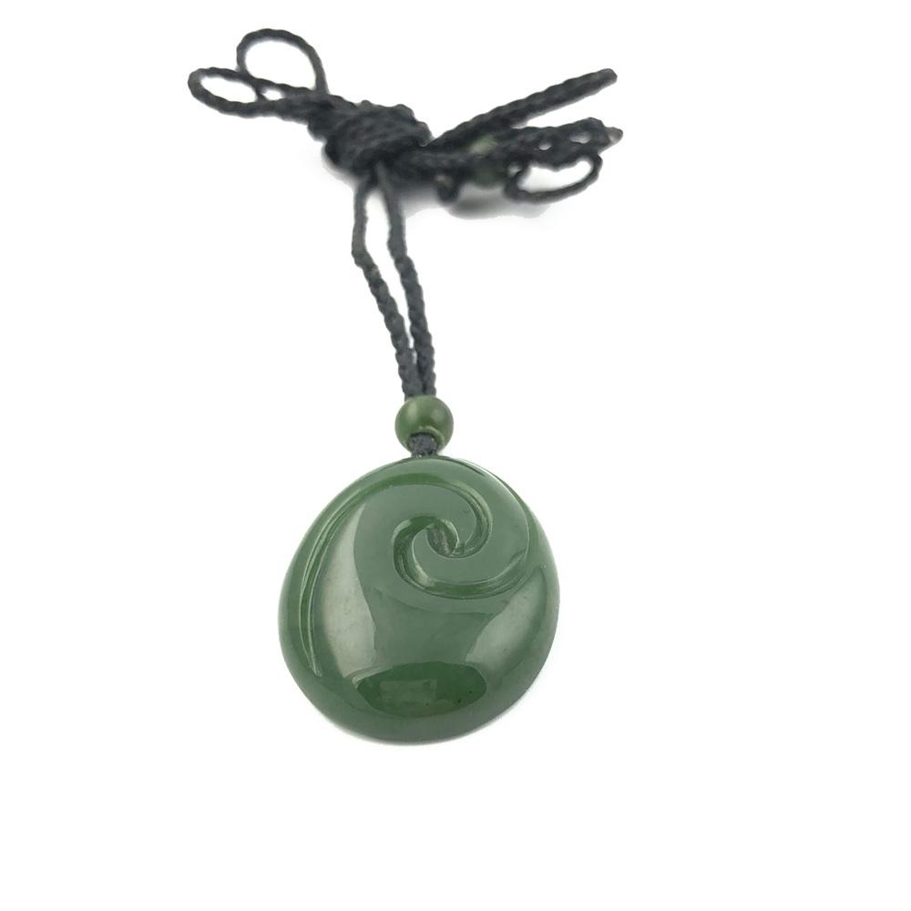 Round green jade pendant with carved swirl on a black cord necklace