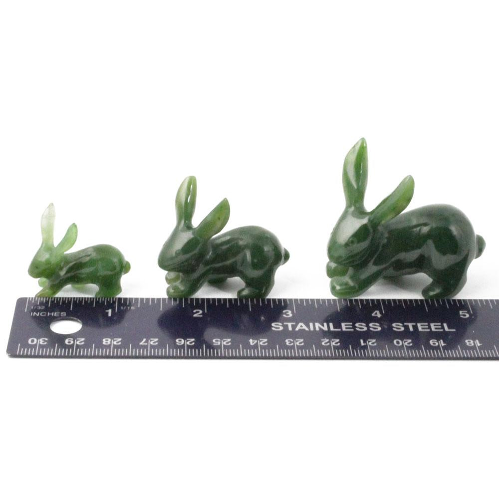 Three green jade jackrabbit carvings arranged by size beside a stainless steel ruler