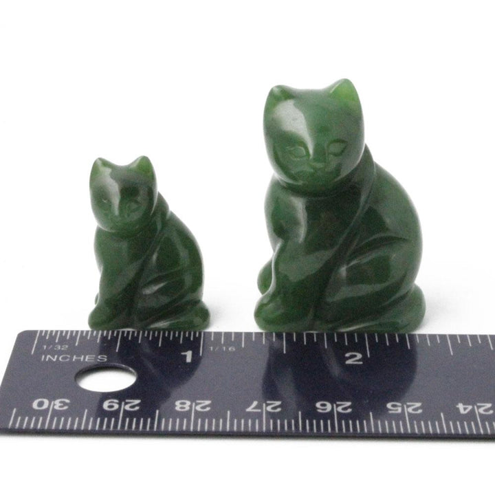 Two green cat figurines of different sizes beside a ruler on a white background
