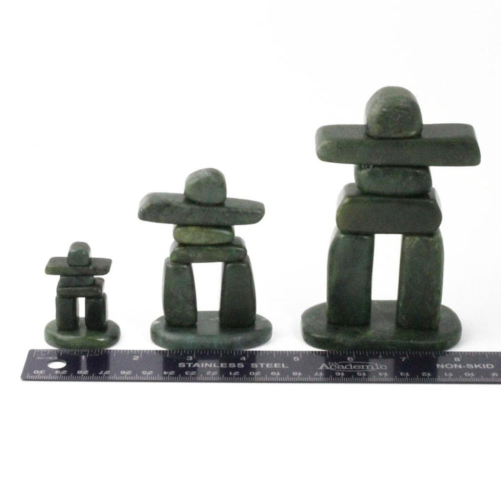 Three green stone Inukshuk figures of different heights arranged in a row with a ruler for scale.