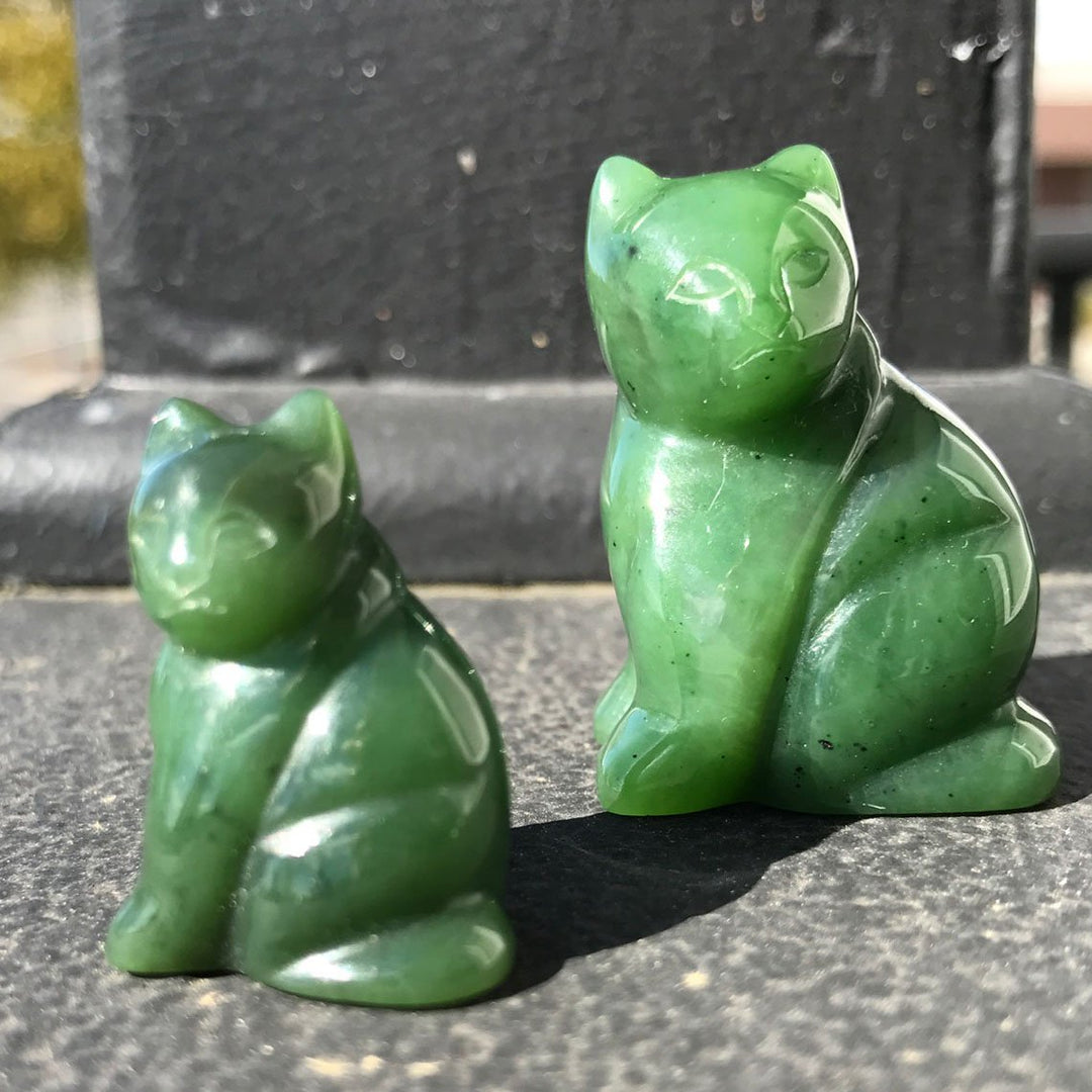 Pair of green jade cat figurines sitting, a larger cat behind a smaller one