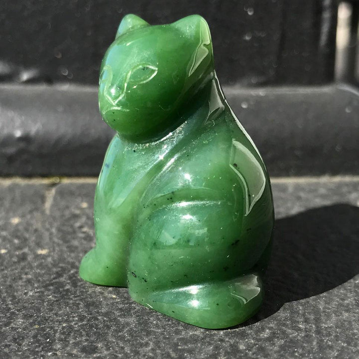 Green carved cat figurine in profile sitting on a dark surface