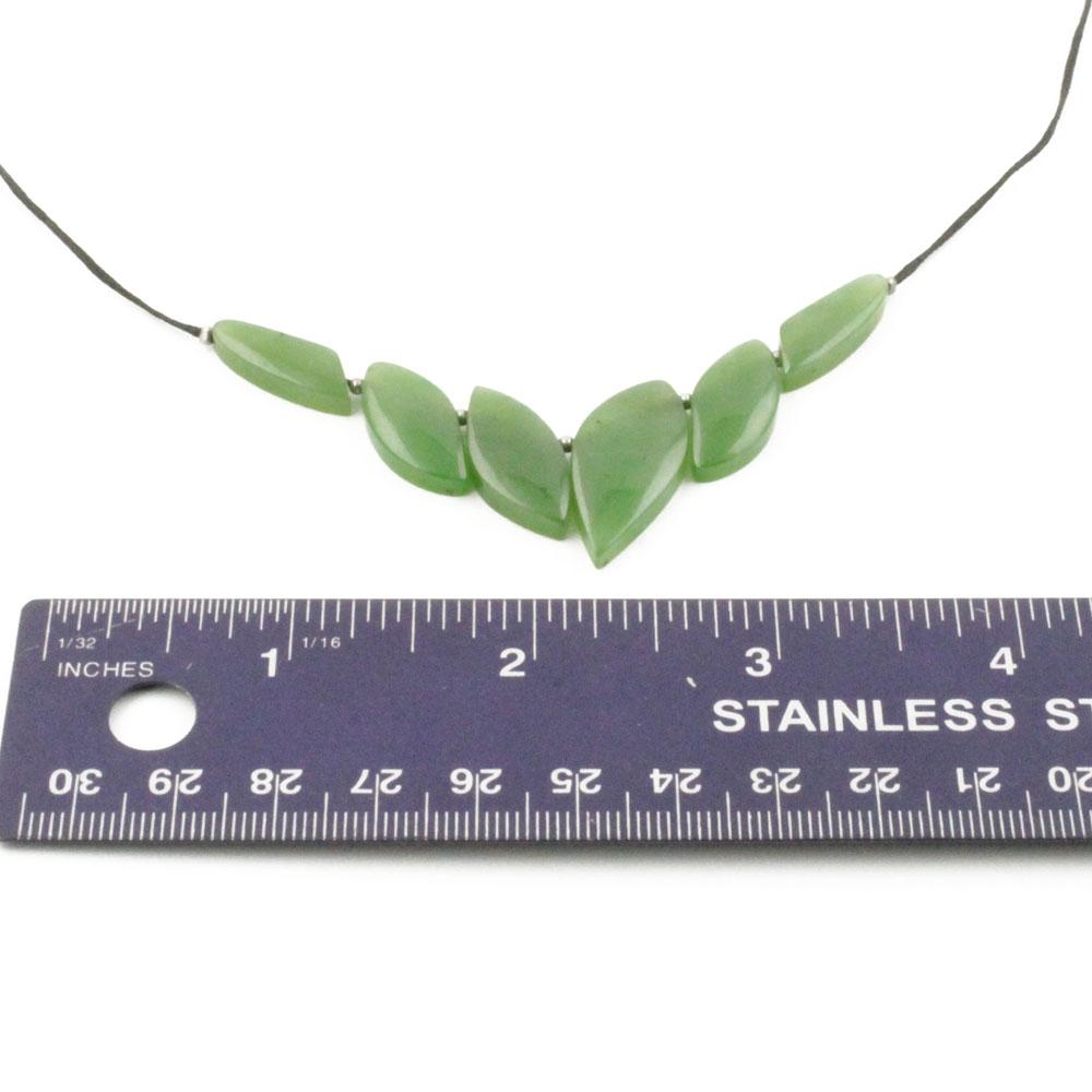Green jade leaf shaped beads form a necklace on a cord with a ruler for scale