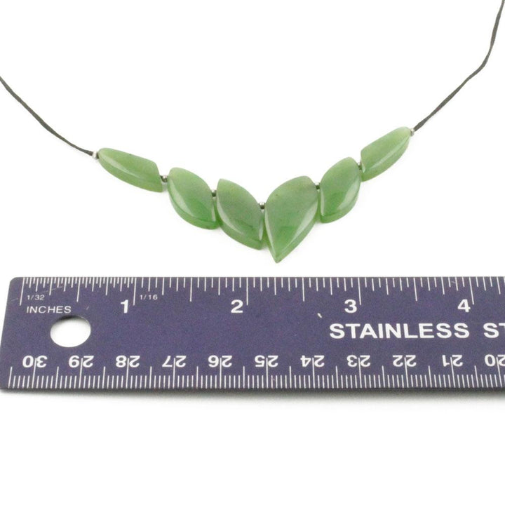 Green jade leaf shaped beads form a necklace on a cord with a ruler for scale