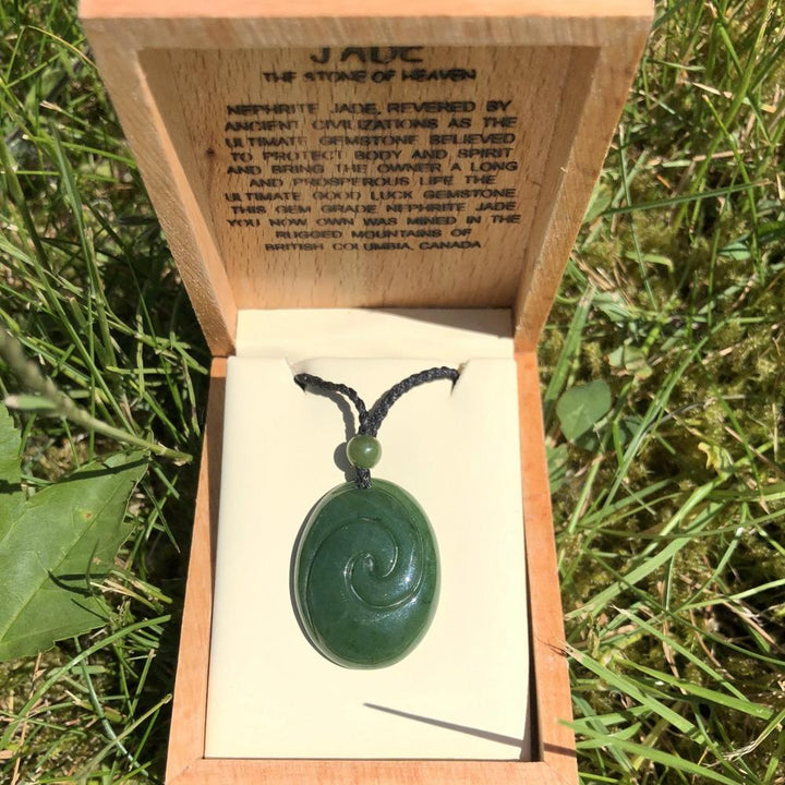 Jade pendant with spiral carving in an open wooden box on a white lining outdoors.