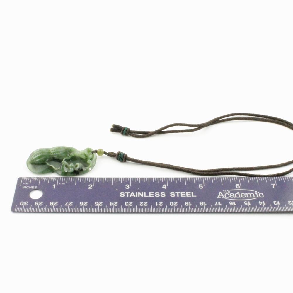 Green jade peanut pendant on brown cord with a small bead, shown beside a ruler for scale