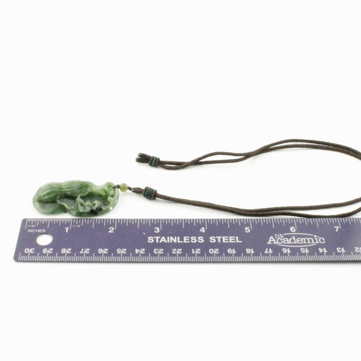 Green jade peanut pendant on brown cord with a small bead, shown beside a ruler for scale