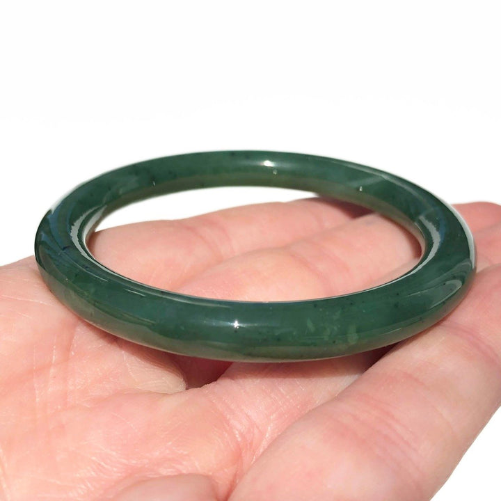 Close up of dark green jade bangle held in hand with white background