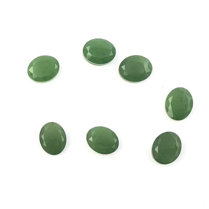 Seven green A Grade 8x10mm faceted cabochons arranged on white background