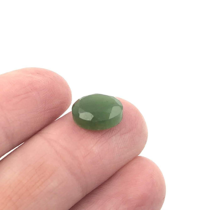 Single green A Grade 8x10mm faceted cabochon held on a fingertip