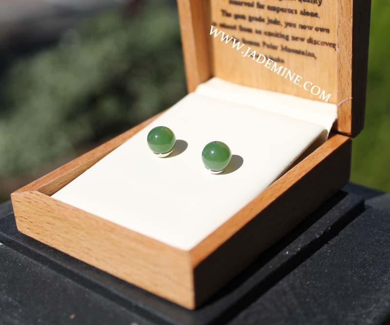 Two green round jade stud earrings in an open wooden jewelry box