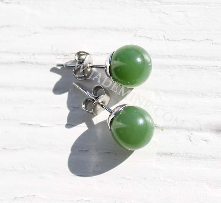 Close-up of green jade round stud earrings with silver posts and butterfly backs on a white surface