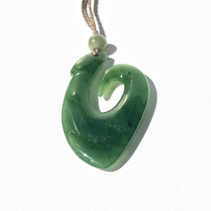 Green jade spiral fish hook pendant on a tan cord against a white background