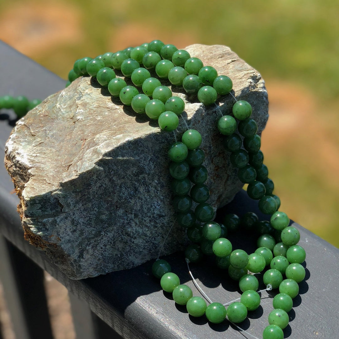 Multiple strands of green 12mm beads draped over a rock outdoors