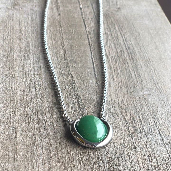 Stainless steel necklace with a green jade pendant resting on a wood surface
