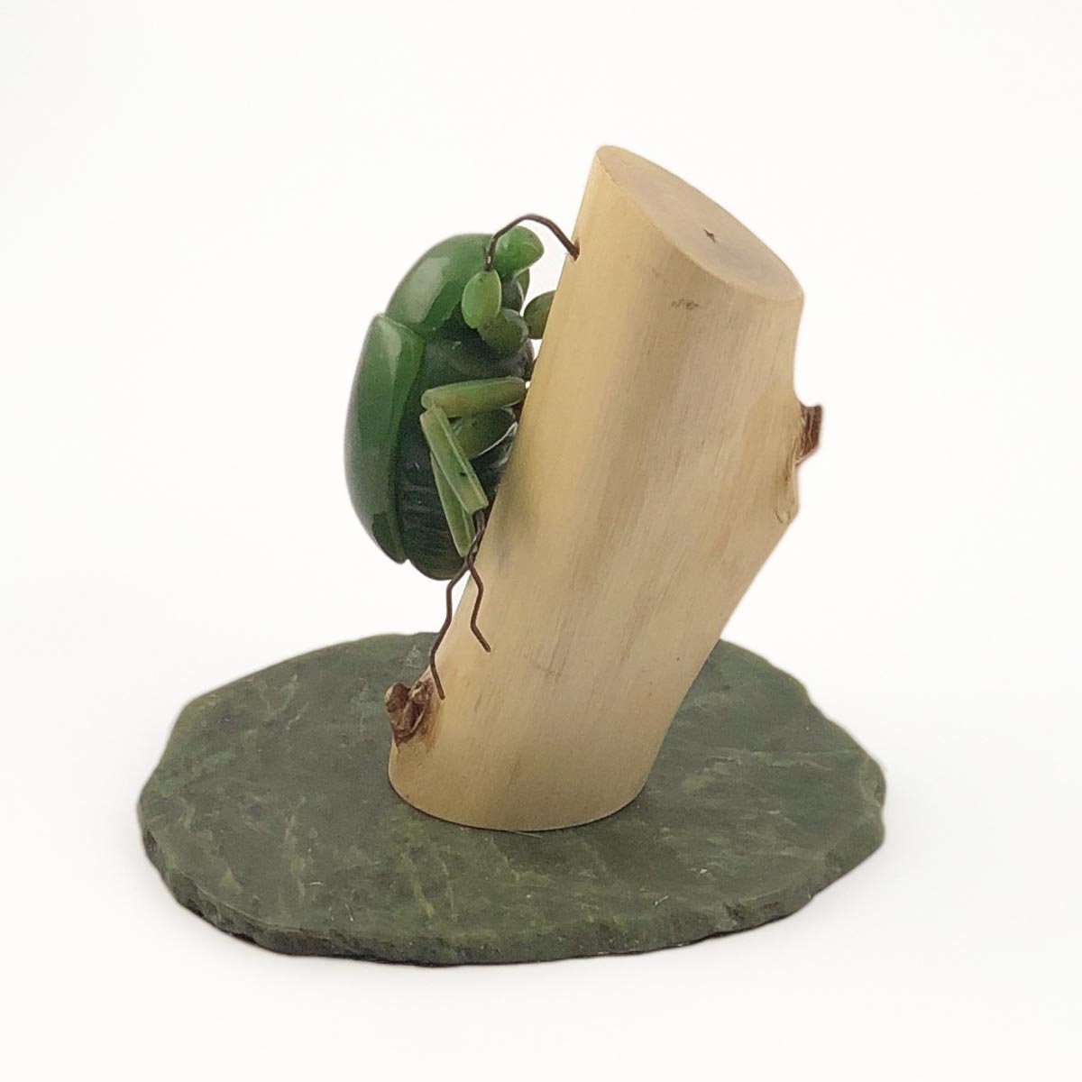 Green jade beetle sculpture perched on a curved light wood block atop a dark green slate base