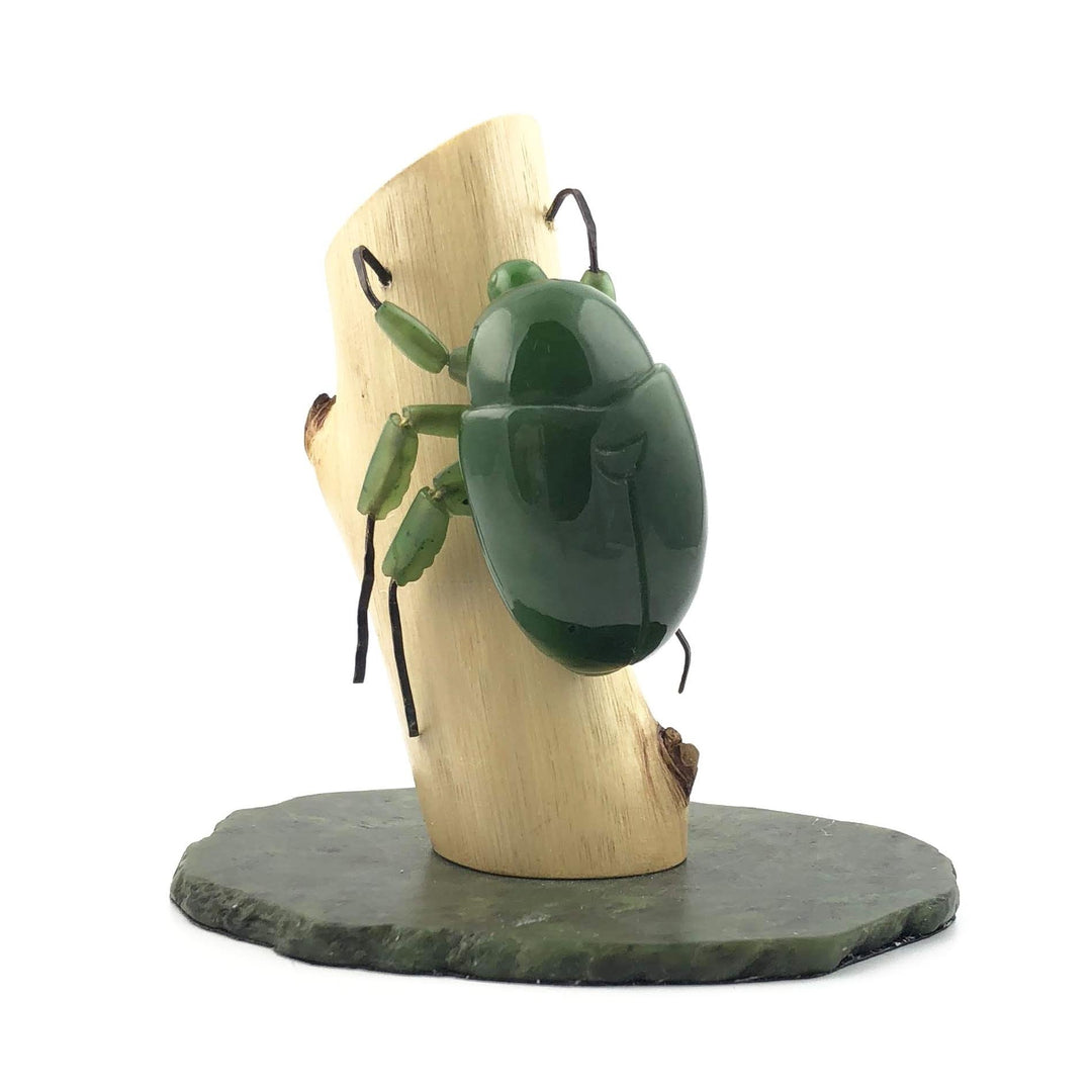 Side view of a glossy green jade beetle attached to a curved light wood block with a slate base