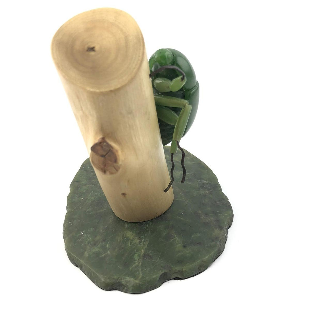 Green jade beetle sculpture mounted on a light wooden log with a dark green stone base
