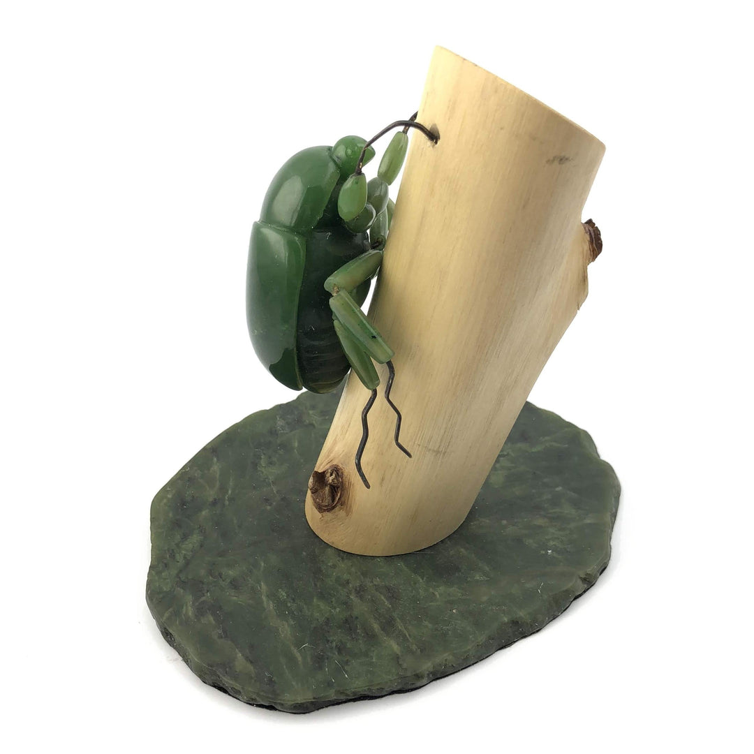 Green jade beetle clinging to a curved light wood log mounted on a dark green stone base