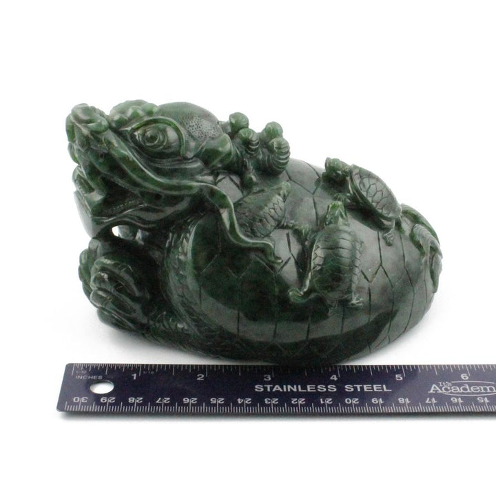 Dark green jade dragon turtle carving with detailed scales and a ruler for scale on a white background