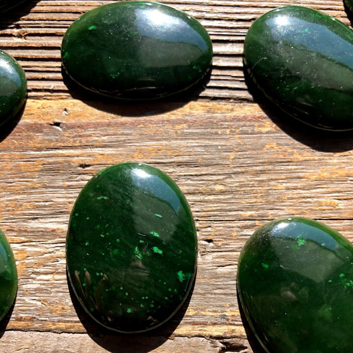 Dark green Cassiar jade cabochons in oval shapes arranged on a weathered wooden surface.