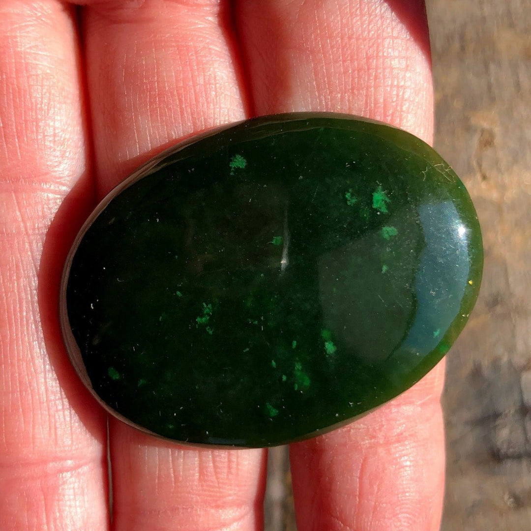 Dark green Cassiar jade cabochon in smooth oval shape held in hand
