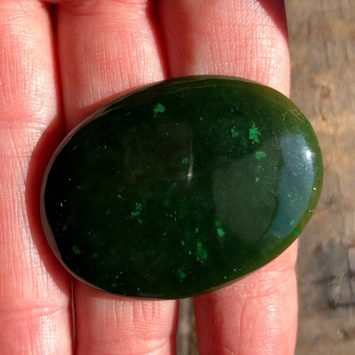 Dark green Cassiar jade cabochon in smooth oval shape held in hand