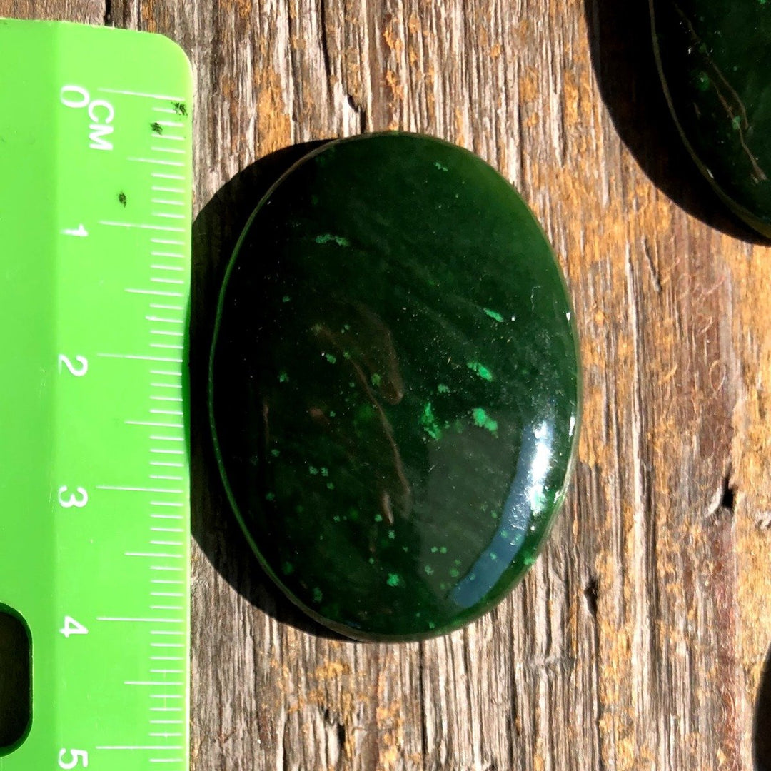 Dark green Cassiar jade cabochon 40x30mm shown beside a ruler for scale