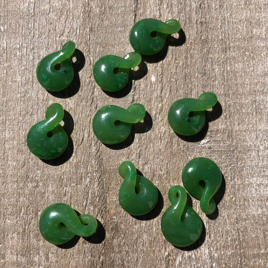 Several small green jade infinity twist beads scattered on a wood surface