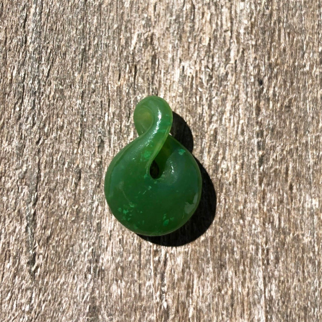 Single green jade infinity twist pendant resting on a wooden surface