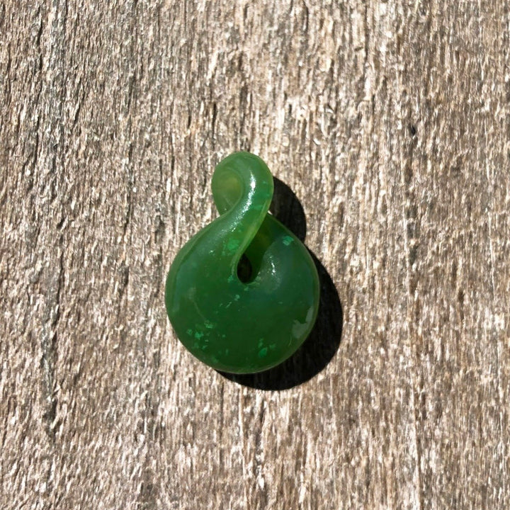 Single green jade infinity twist pendant resting on a wooden surface