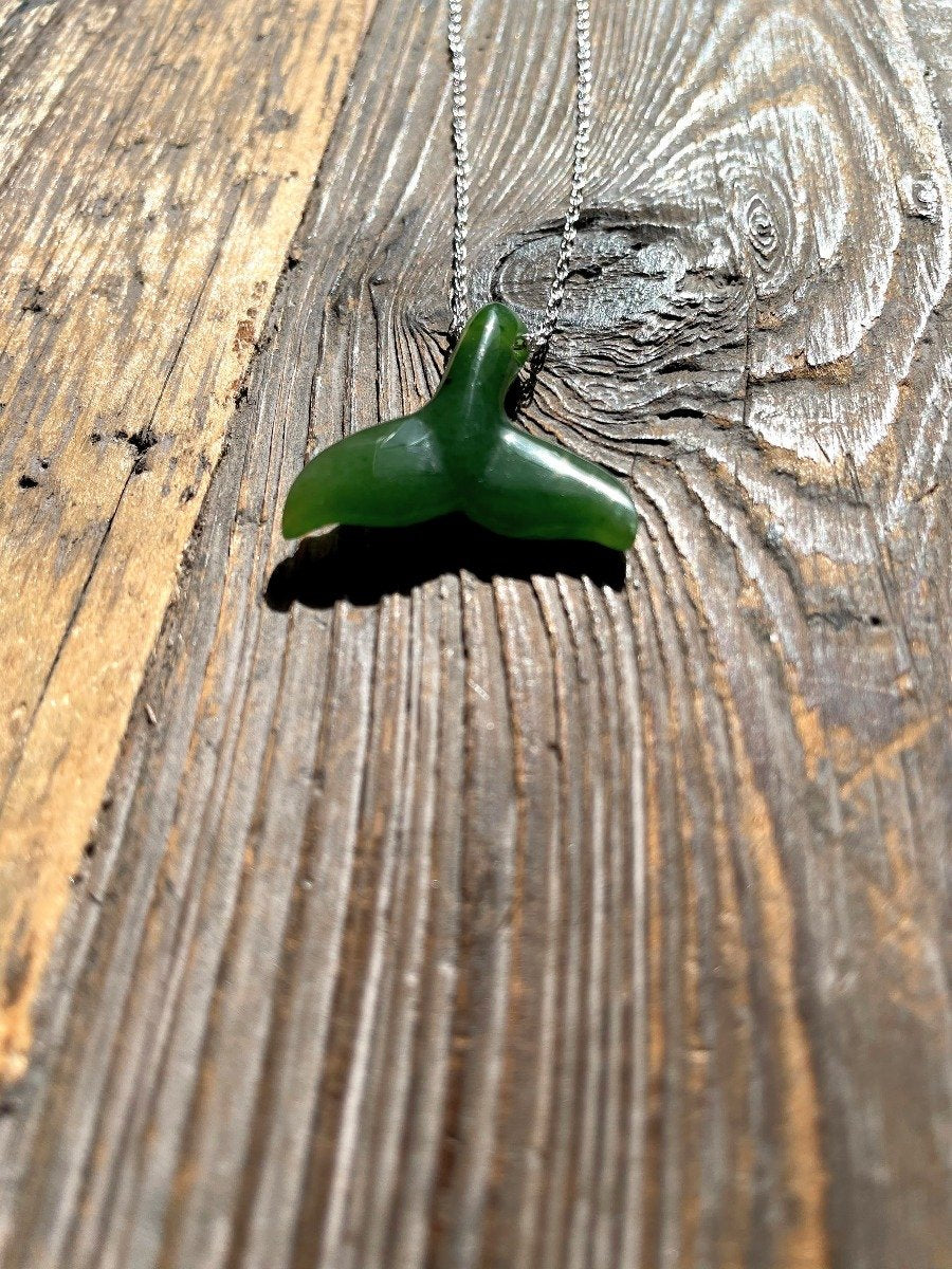 Green whale tail pendant on a silver chain resting on a rustic wooden surface