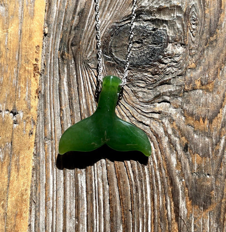 Green whale tail pendant on a silver chain against a weathered wooden background