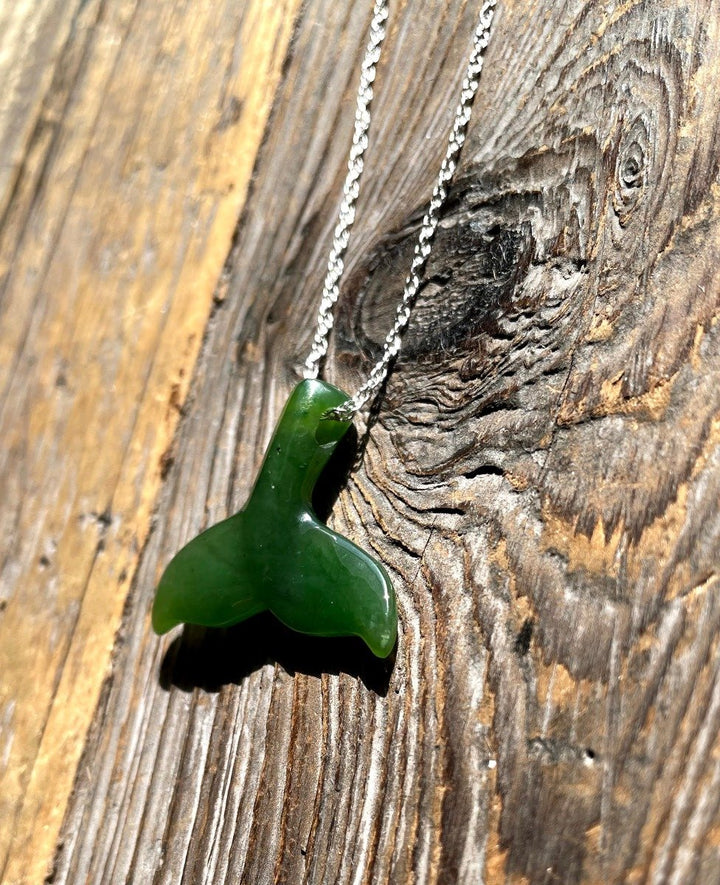 Green whale tail pendant on a silver chain displayed on weathered wood texture