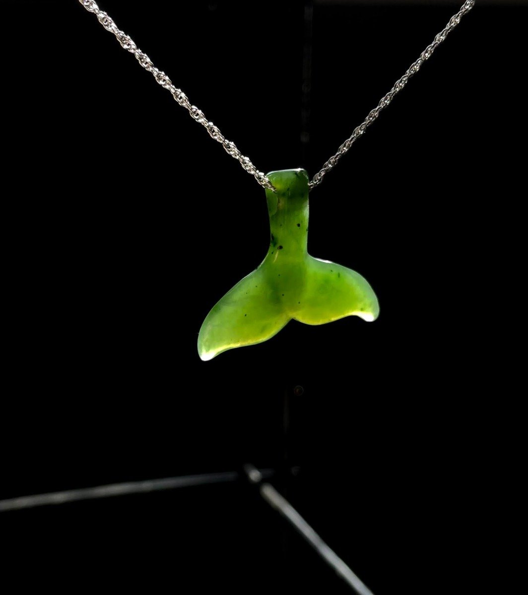 Green whale tail pendant suspended on a silver chain against a black background