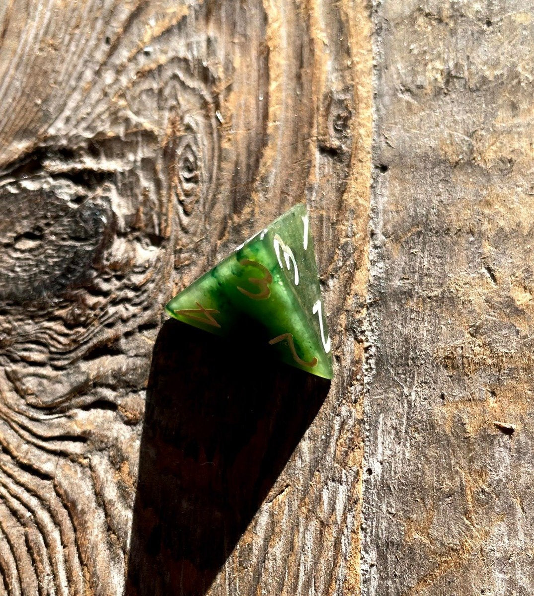 Green jade D4 die resting on weathered wood with white digits visible