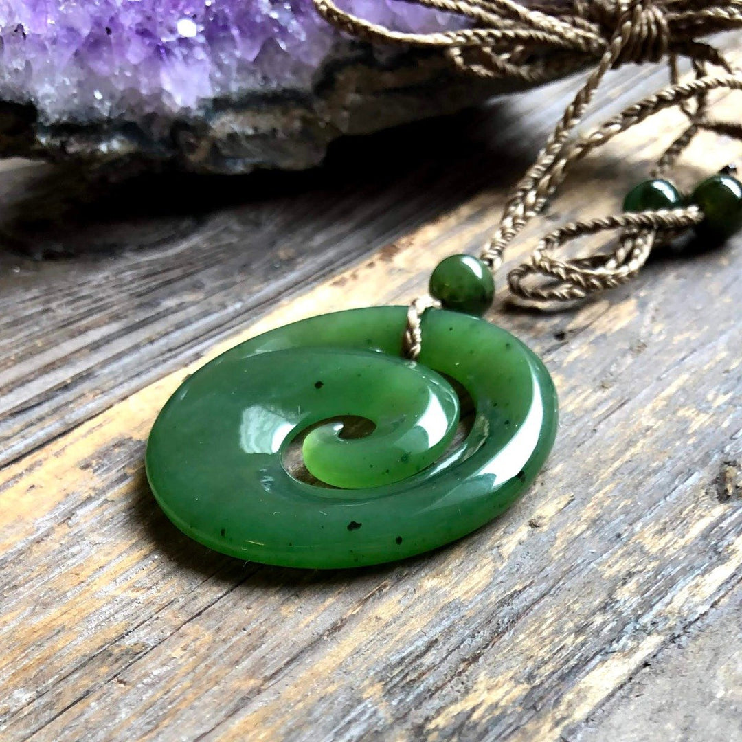 Green spiral koru pendant with a small bead on a braided cord resting on a wooden surface