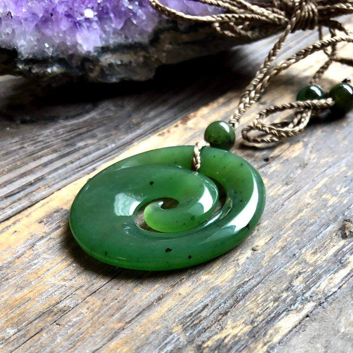 Green spiral koru pendant with a small bead on a braided cord resting on a wooden surface