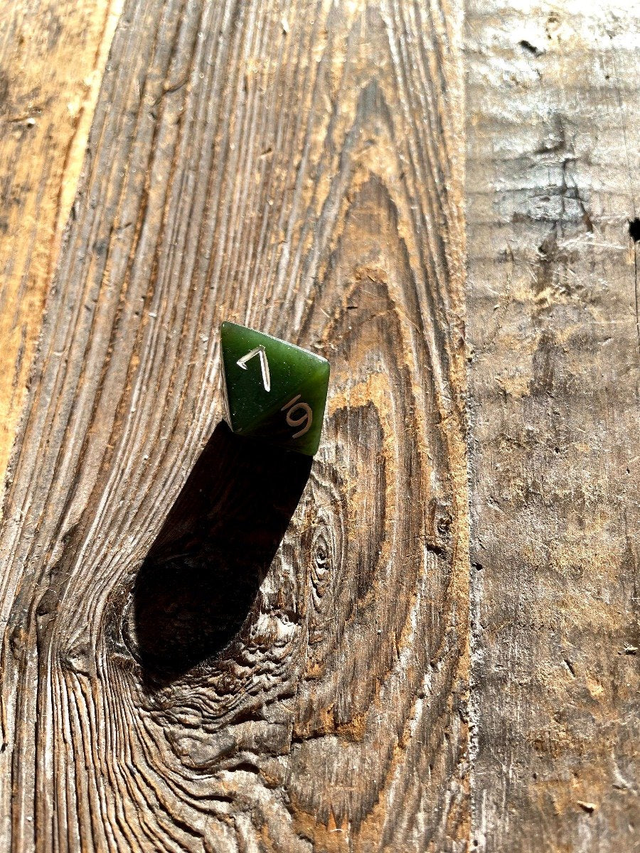 Green jade D8 die with white numbers on a rough wooden background.