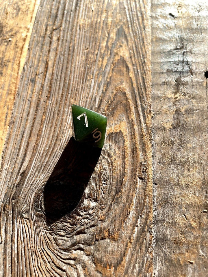 Green jade D8 die with white numbers on a rough wooden background.