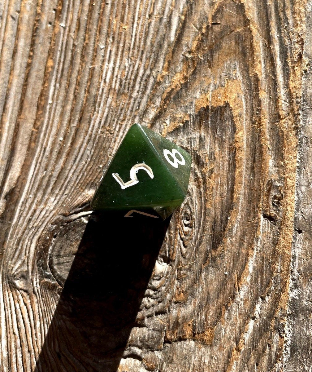 Green jade D8 die with white numbers visible on a weathered wooden surface showing 5 and 8.